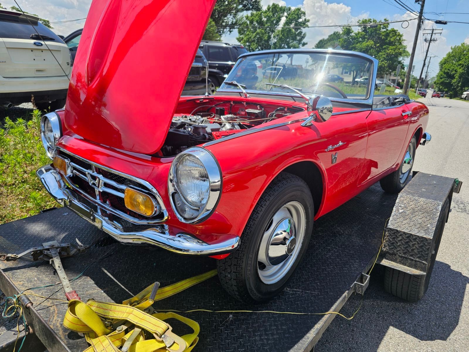 A red car with the hood up is on a trailer.