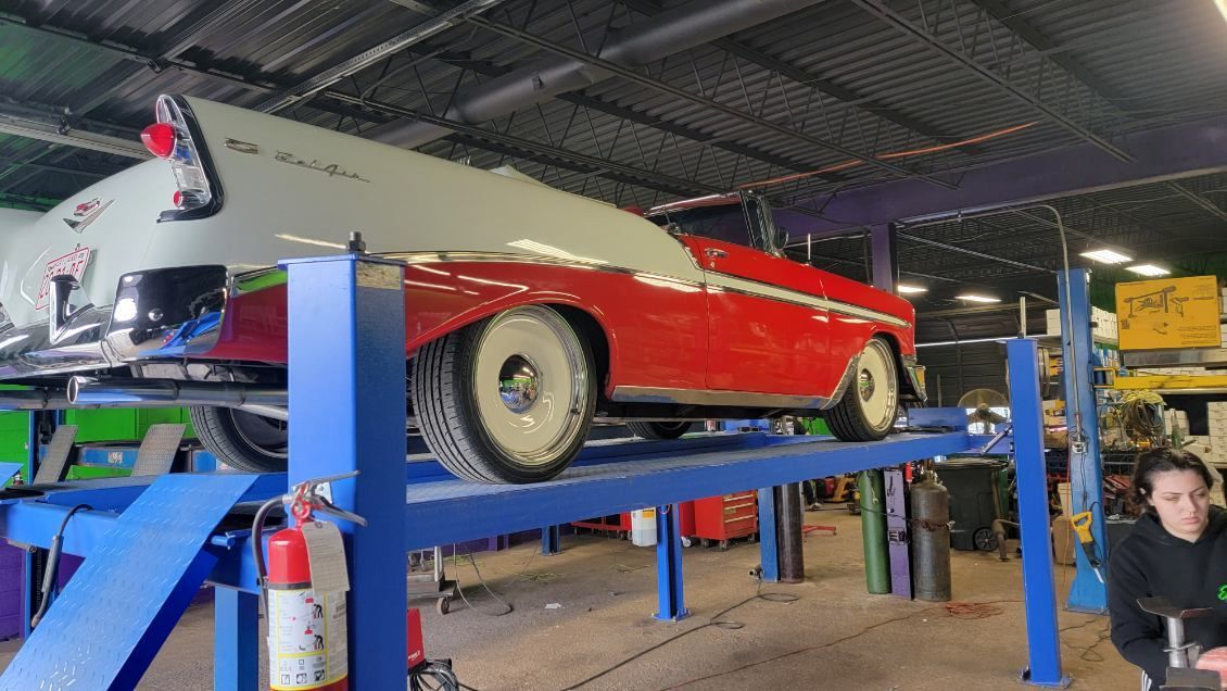 A red and white car is on a lift in a garage.