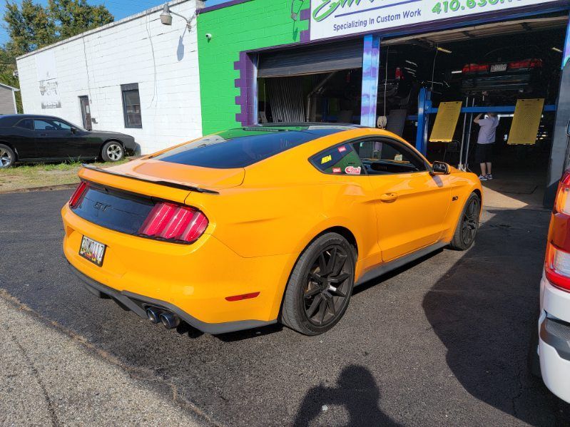A yellow mustang is parked in front of a garage.