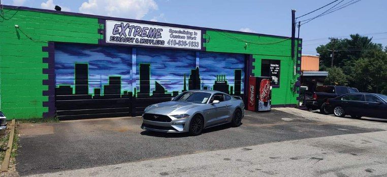 A gray mustang is parked in front of a green building.