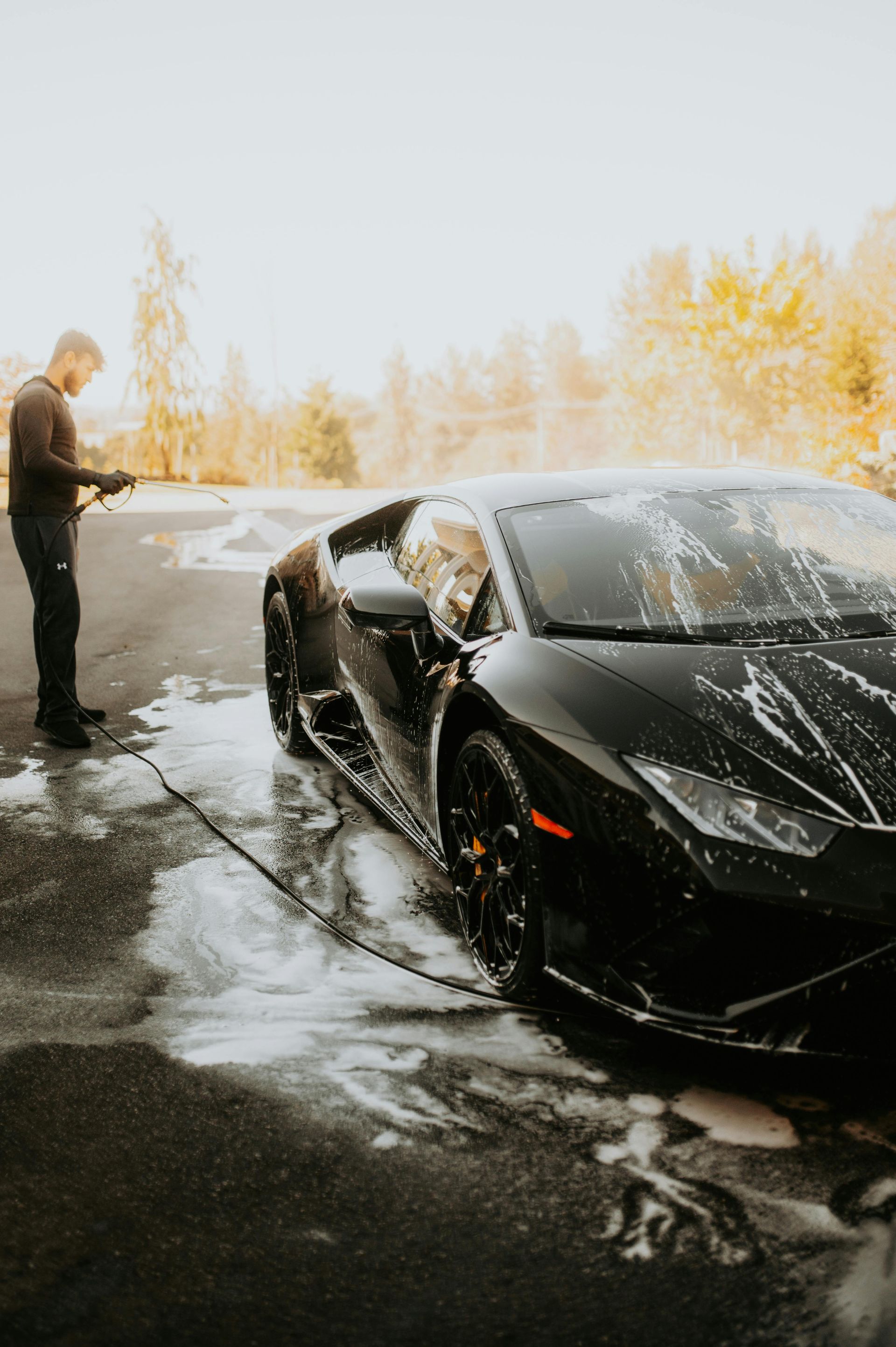 A man is washing a black sports car with a high pressure washer.