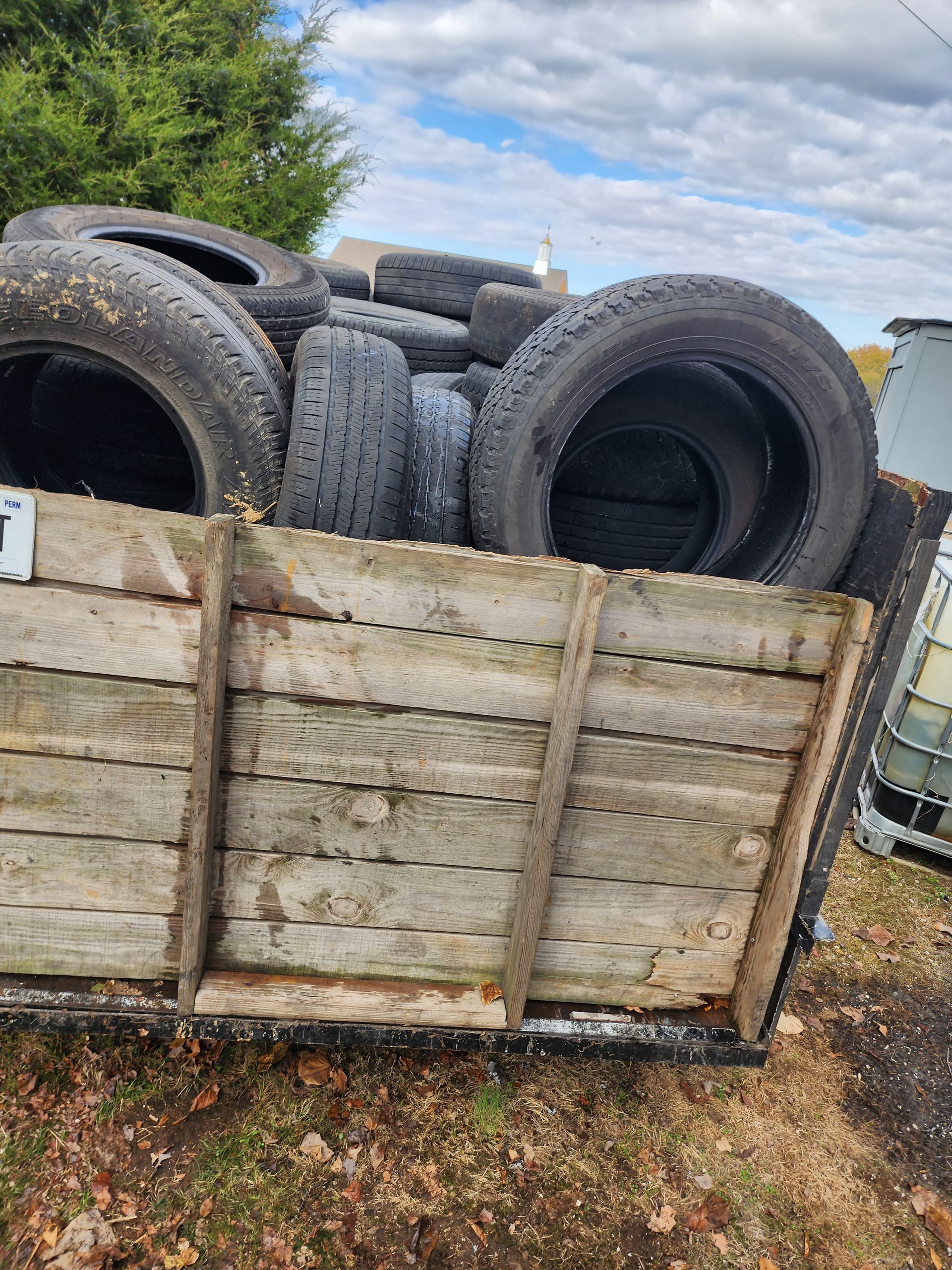 Tires piled in a wooden trailer, set against a cloudy sky.