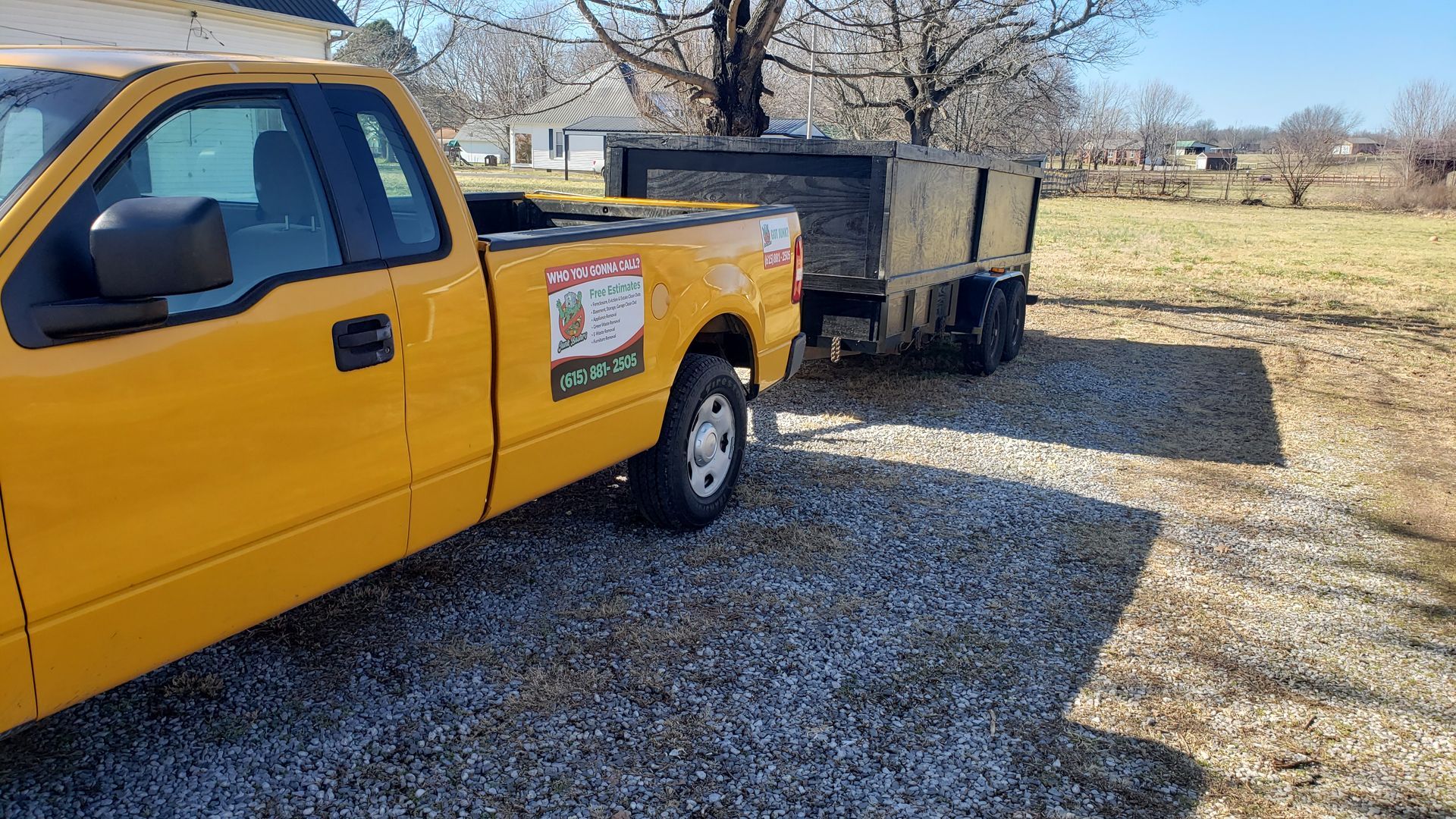 Yellow truck towing a trailer on gravel; parked outdoors on a sunny day.