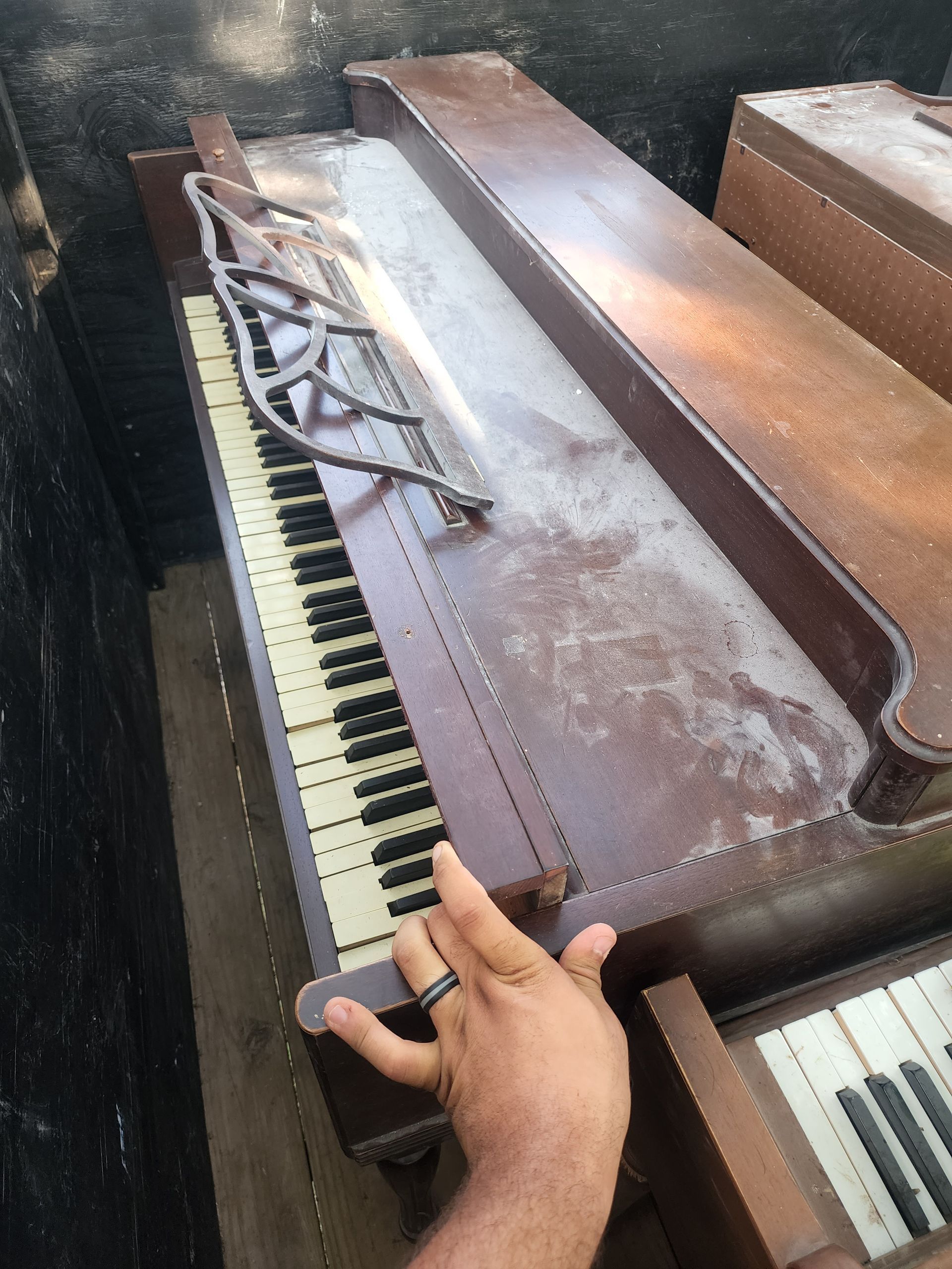 Damaged upright piano in a dumpster, with broken keys and a person's hand visible.