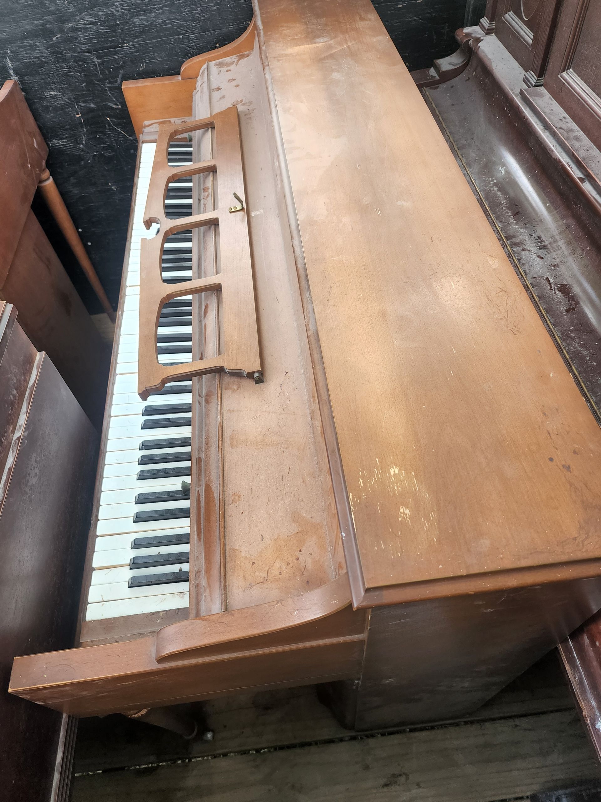 Wooden upright piano with white and black keys, damaged and weathered.