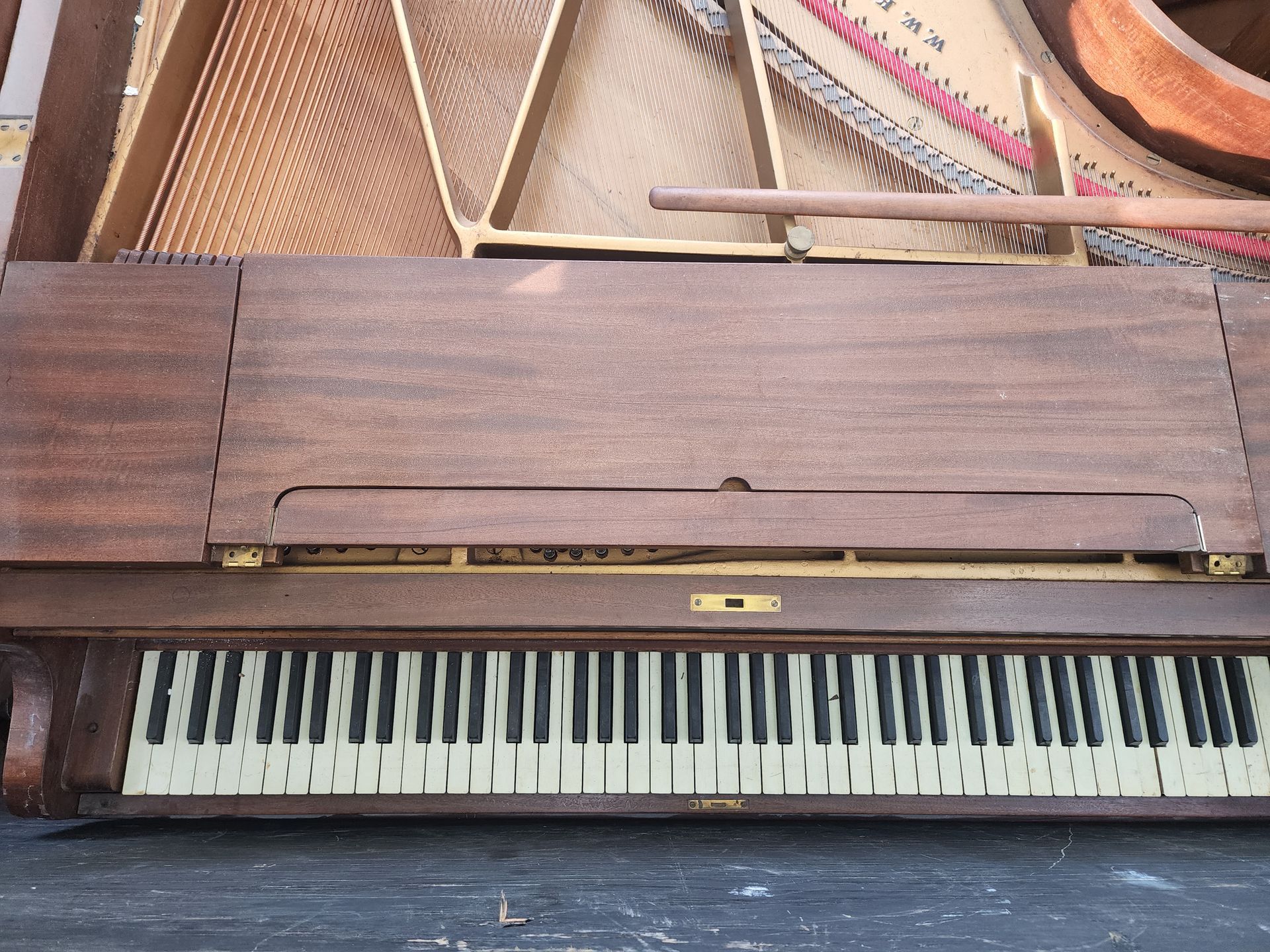 Wooden upright piano with ivory-colored keys; the top is open, revealing strings and wood.