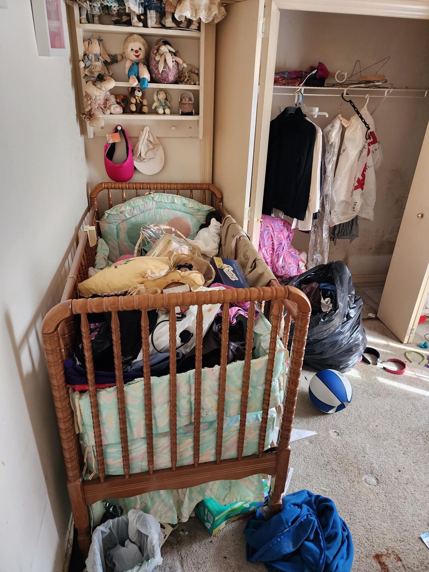 A baby crib is sitting in a messy room next to a closet.