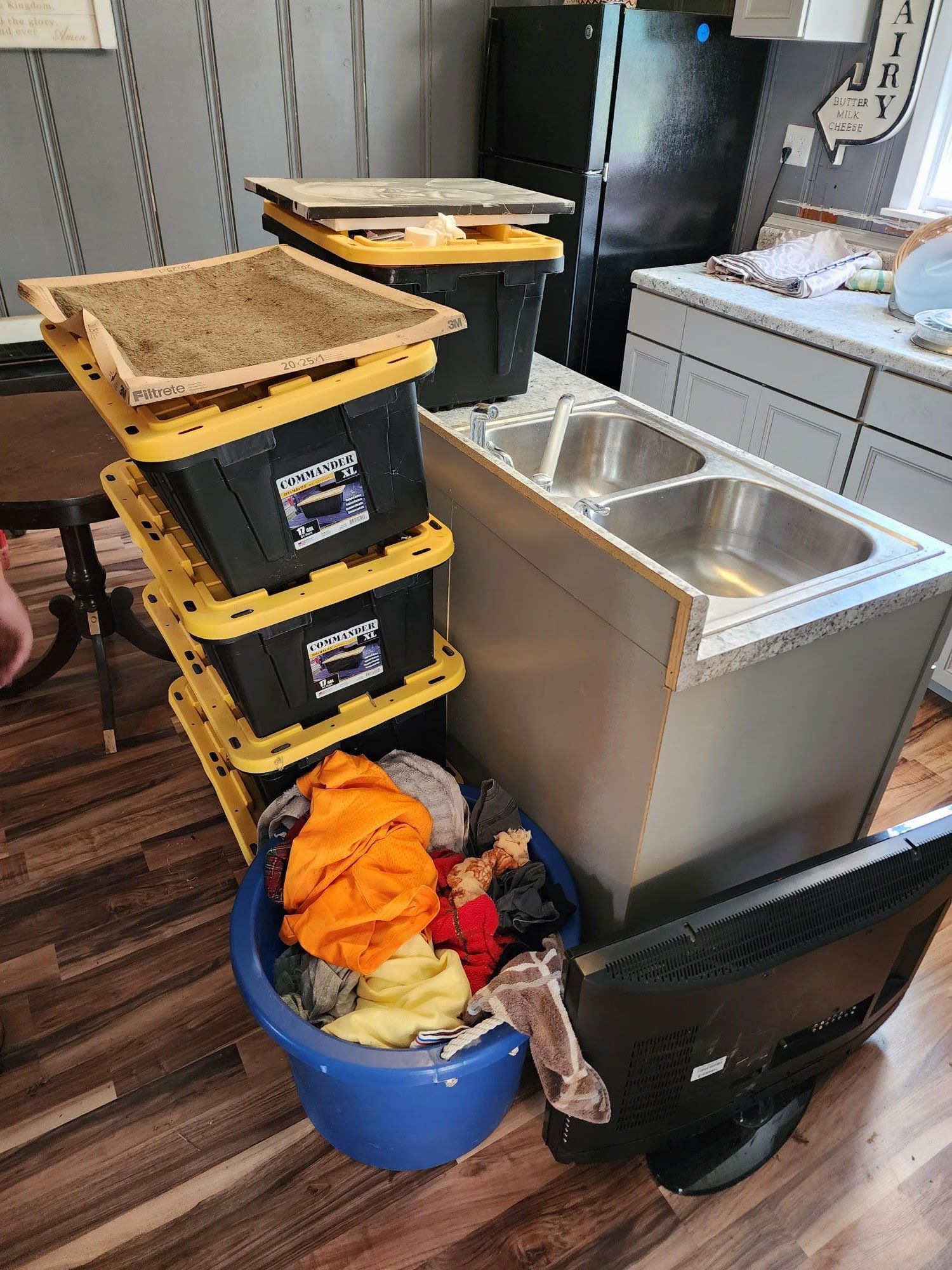 A kitchen with a sink , a television , and a stack of plastic bins.