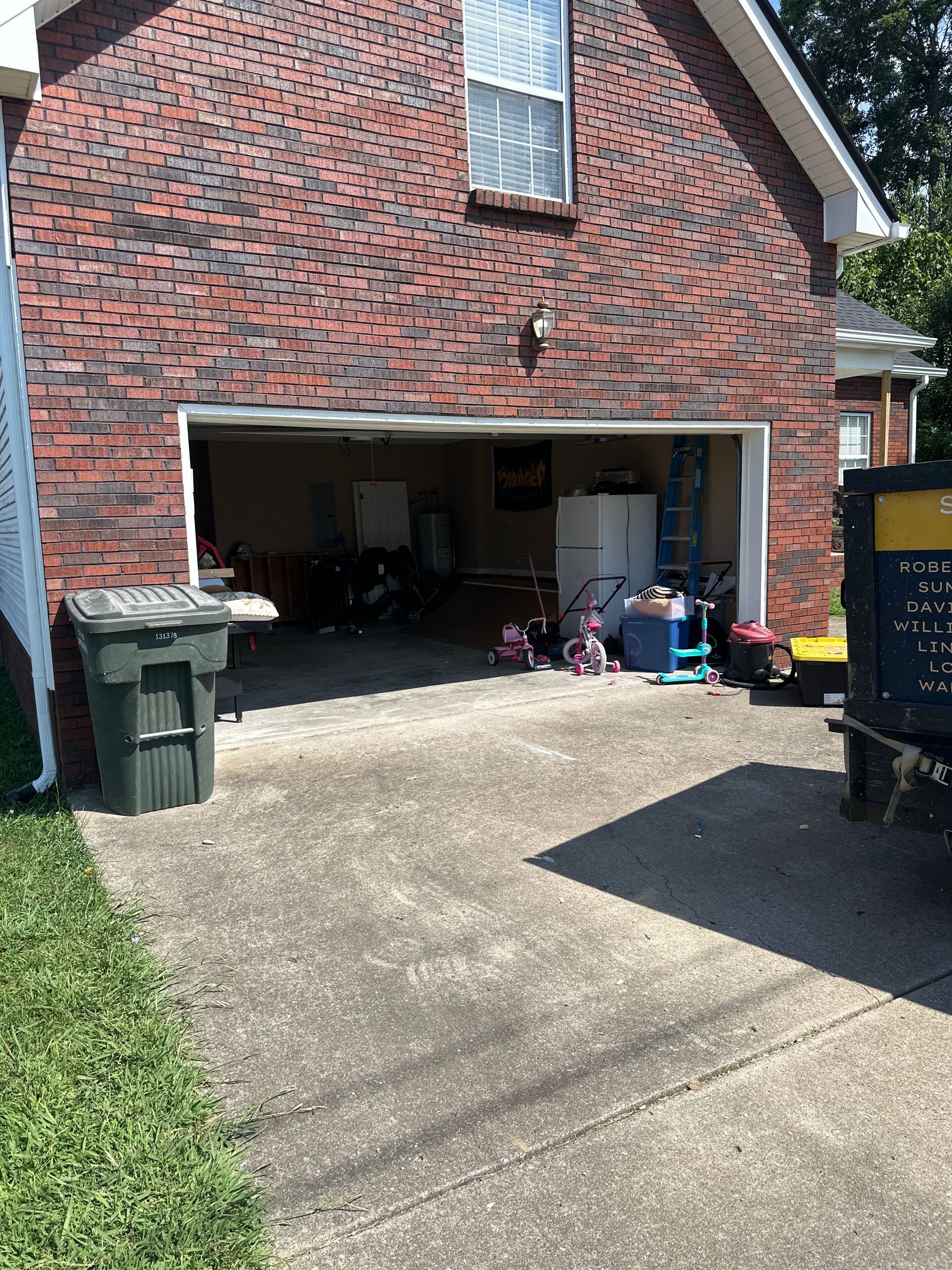 A brick garage with a trash can in front of it.