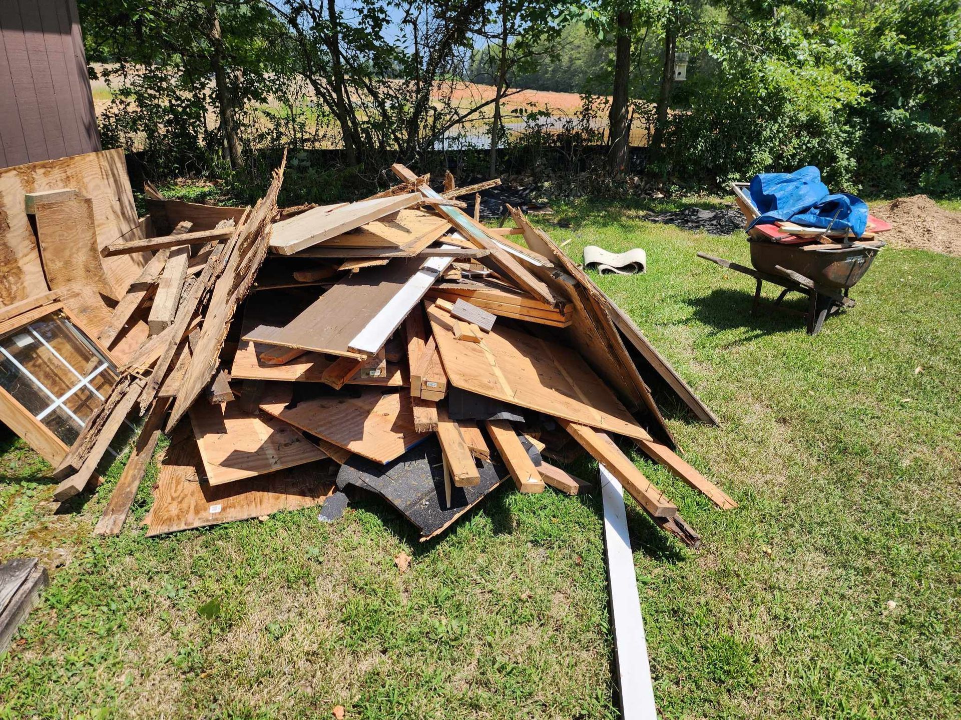 A pile of wood is sitting on the grass next to a wheelbarrow.