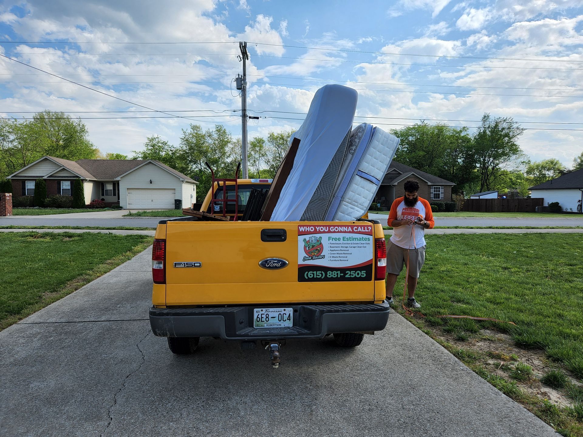 Yellow pickup truck loaded with furniture, man standing nearby on a driveway, suburban setting.