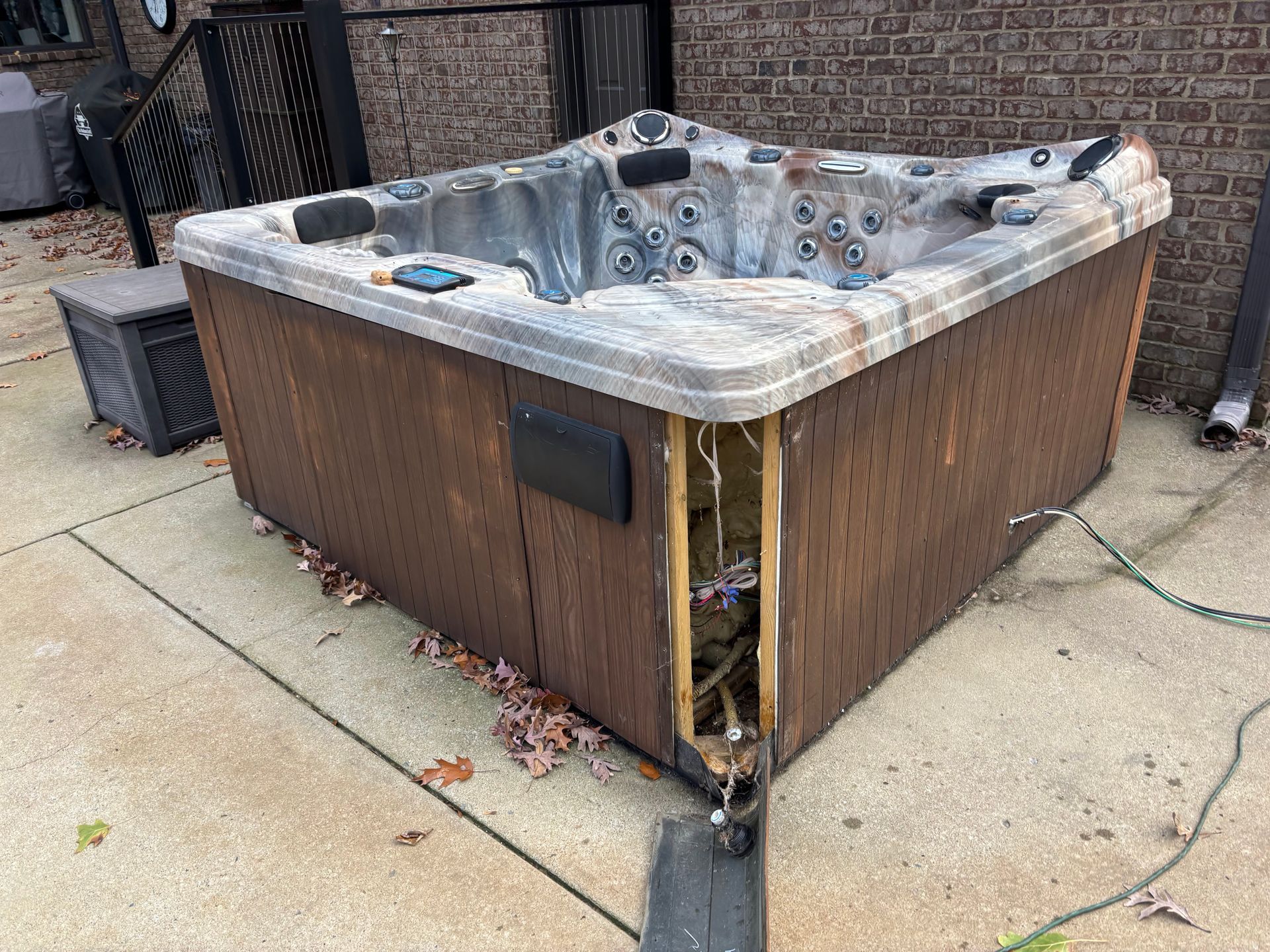 Damaged hot tub with missing side panel on a concrete patio.