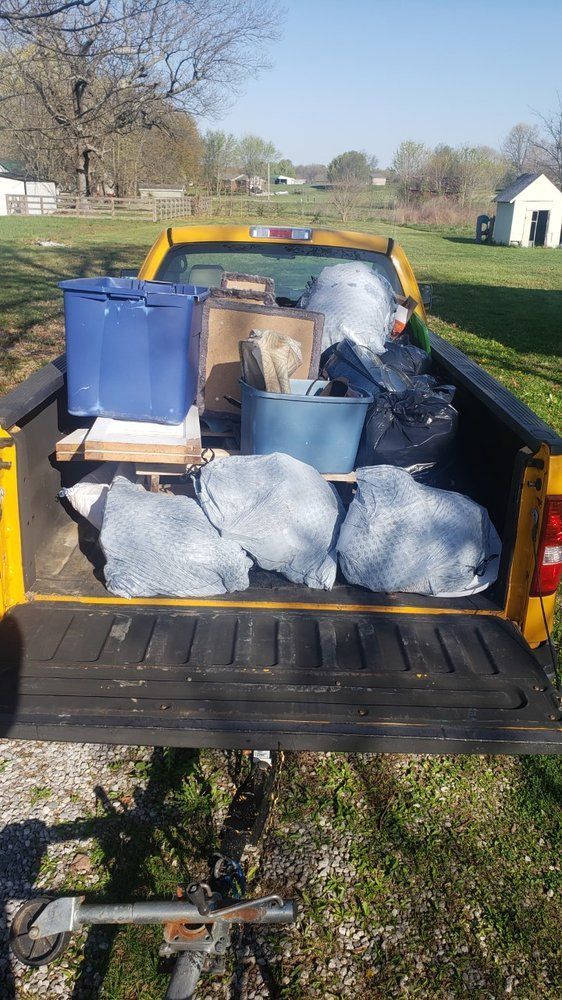 The back of a yellow truck is filled with lots of trash.