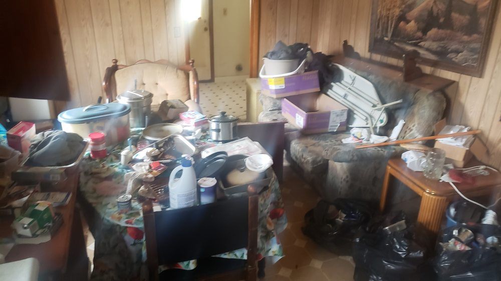 A messy room with a table , chairs , boxes and trash bags.