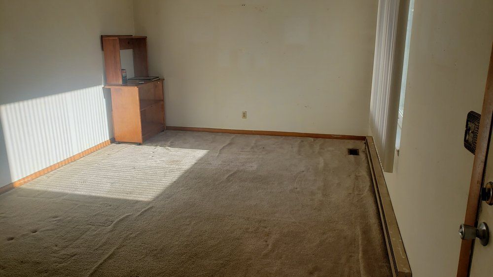 An empty living room with a carpeted floor and a window.