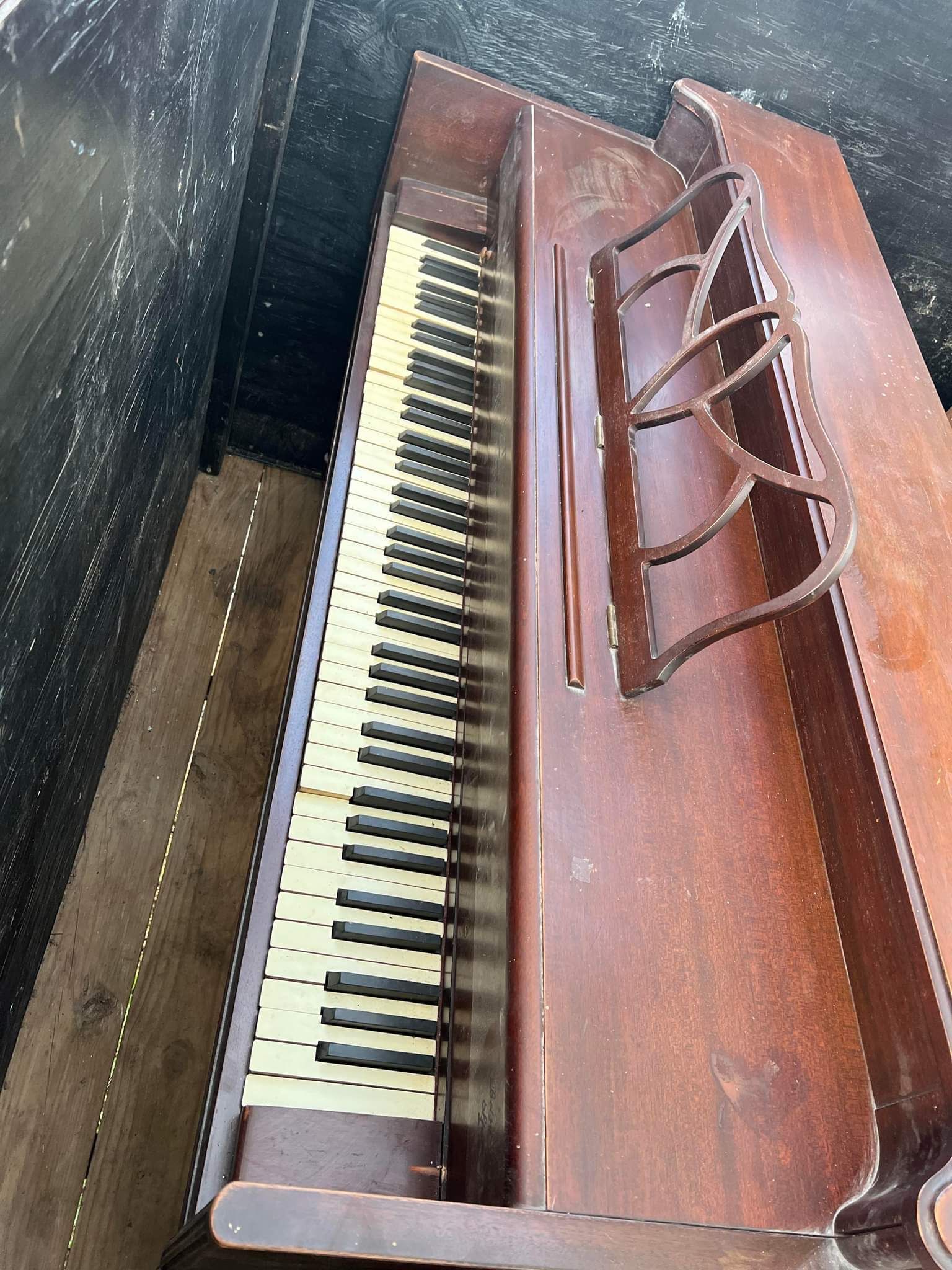 Wooden organ with ivory keys, in a dark setting. Music stand attached to the right side.