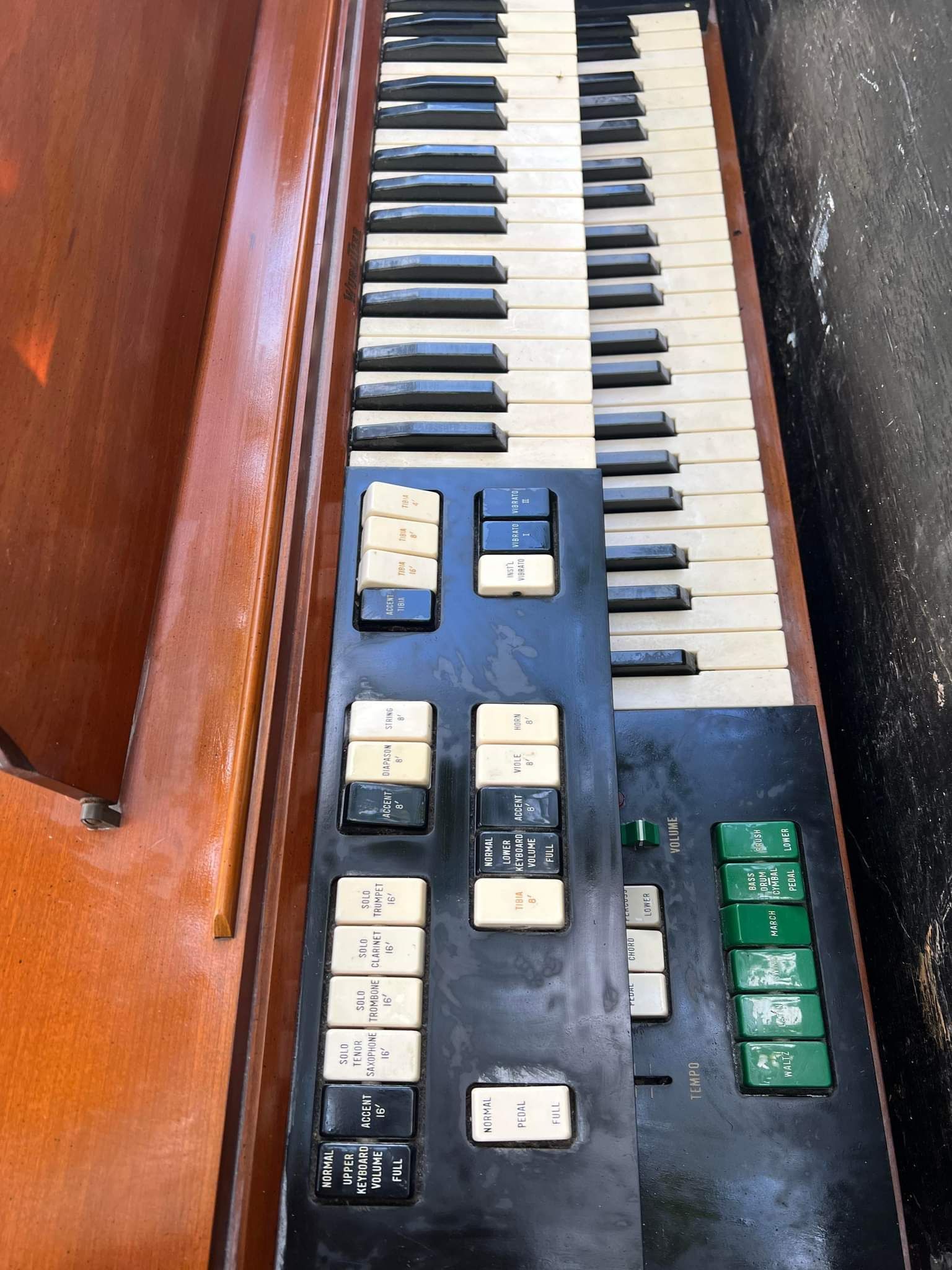 Close-up of a vintage organ keyboard with multiple rows of white and black keys, various black and green buttons.