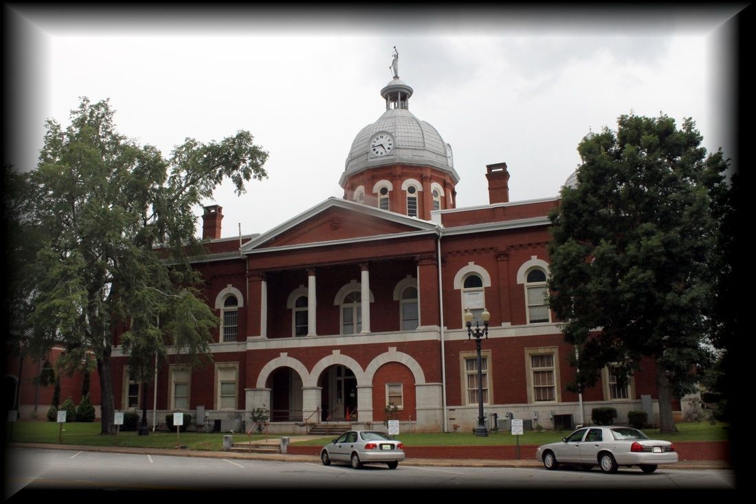 Red brick courthouse with white arched entrances, a pillared porch, and a central domed clock tower under a cloudy sky.