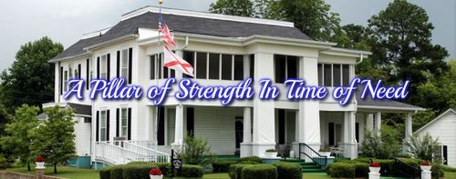 A white two-story historic house with a large front porch and columns, displaying the text 