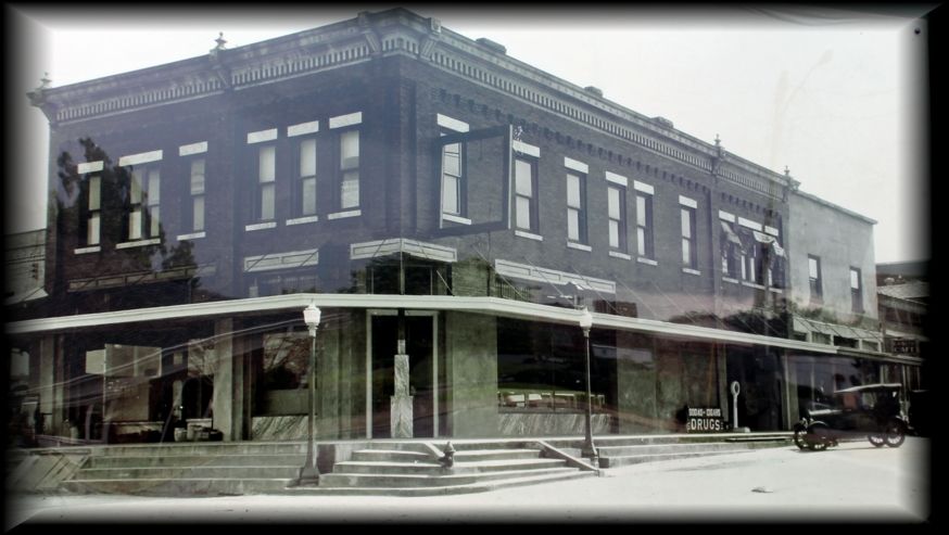 A vintage, street-level view of a dark-colored, two-story commercial building with a modern glass entrance and canopy.