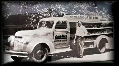 A vintage delivery truck for Lime-Cola with a person standing beside it in an outdoor setting.