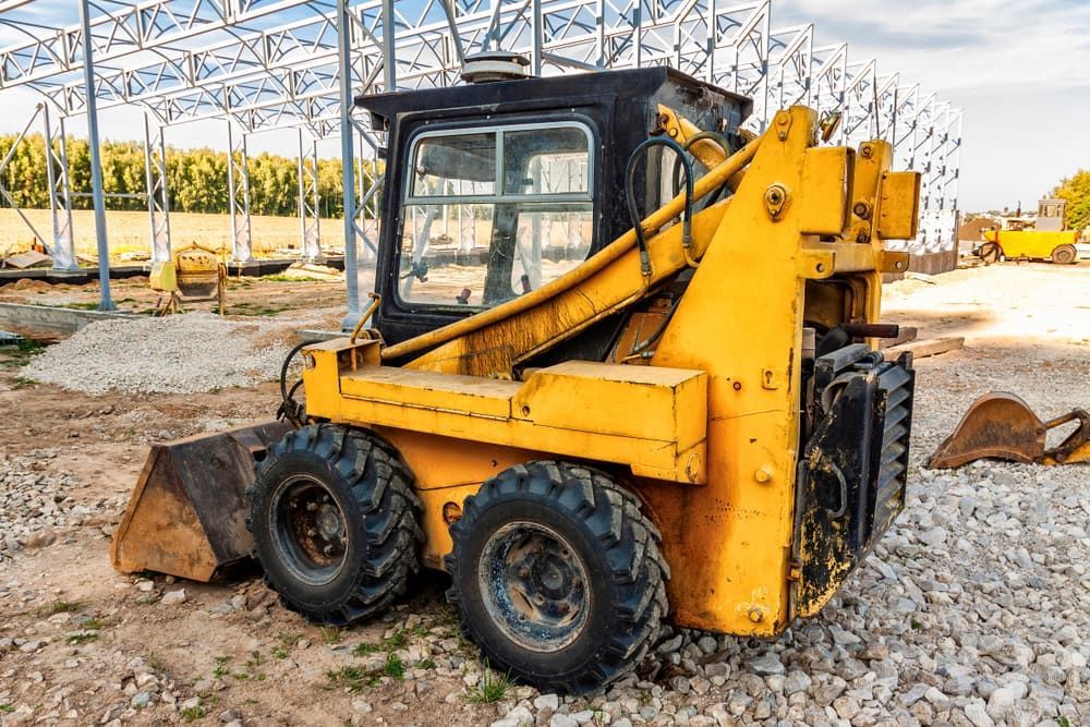 A Yellow Skid Steer Loader Is Parked on A Gravel Road at A Construction Site — Glass in Wollongong, NSW