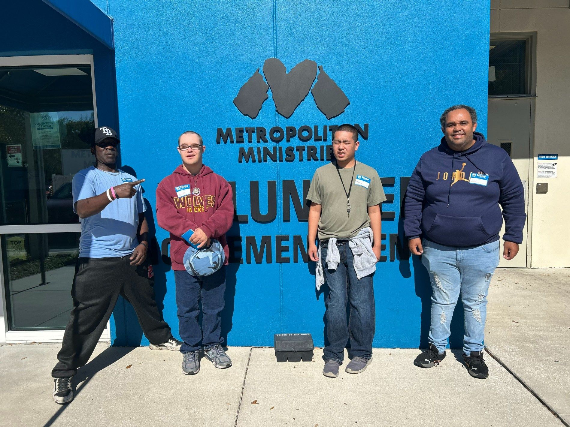 Four people standing outside a blue wall with a Metropolitan Ministries sign