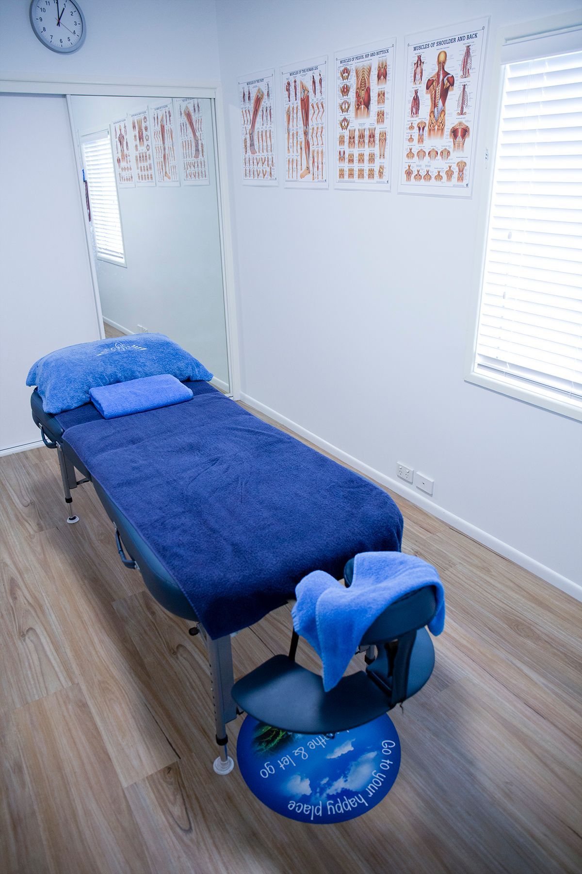 A Massage Table In A Room With A Chair And A Clock On The Wall – Chermside, QLD - Hands From Heaven Remedial Therapy Clinic