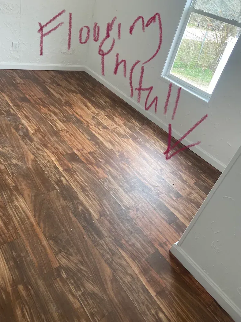 Room with wood-look flooring and graffiti on the white wall: 