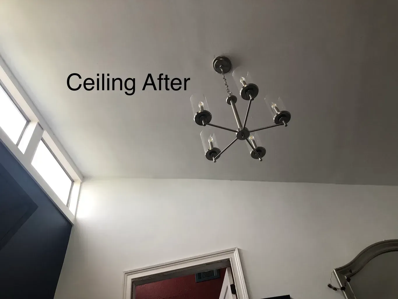 White ceiling with modern chandelier; windows on the left; doorway and mirror below.