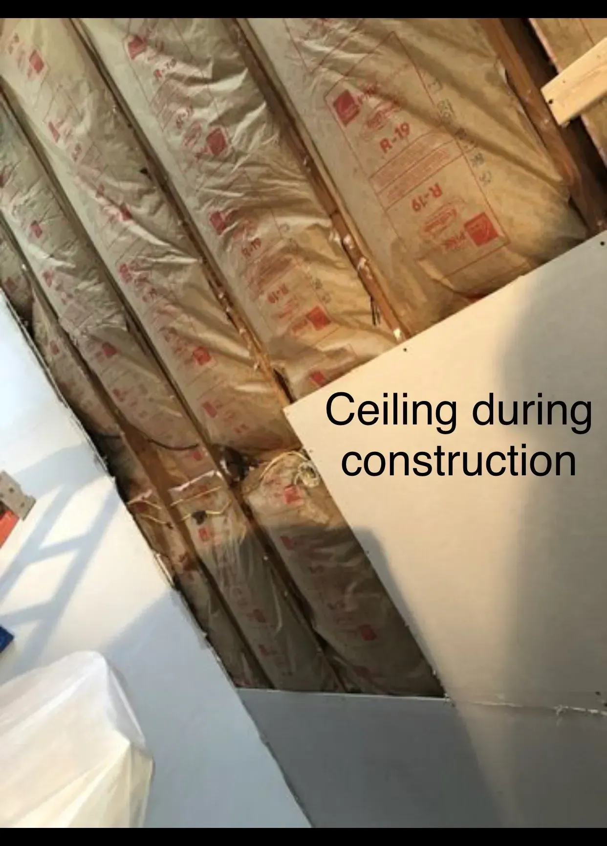 Ceiling under construction: insulation between beams, drywall partially installed, bright lighting.