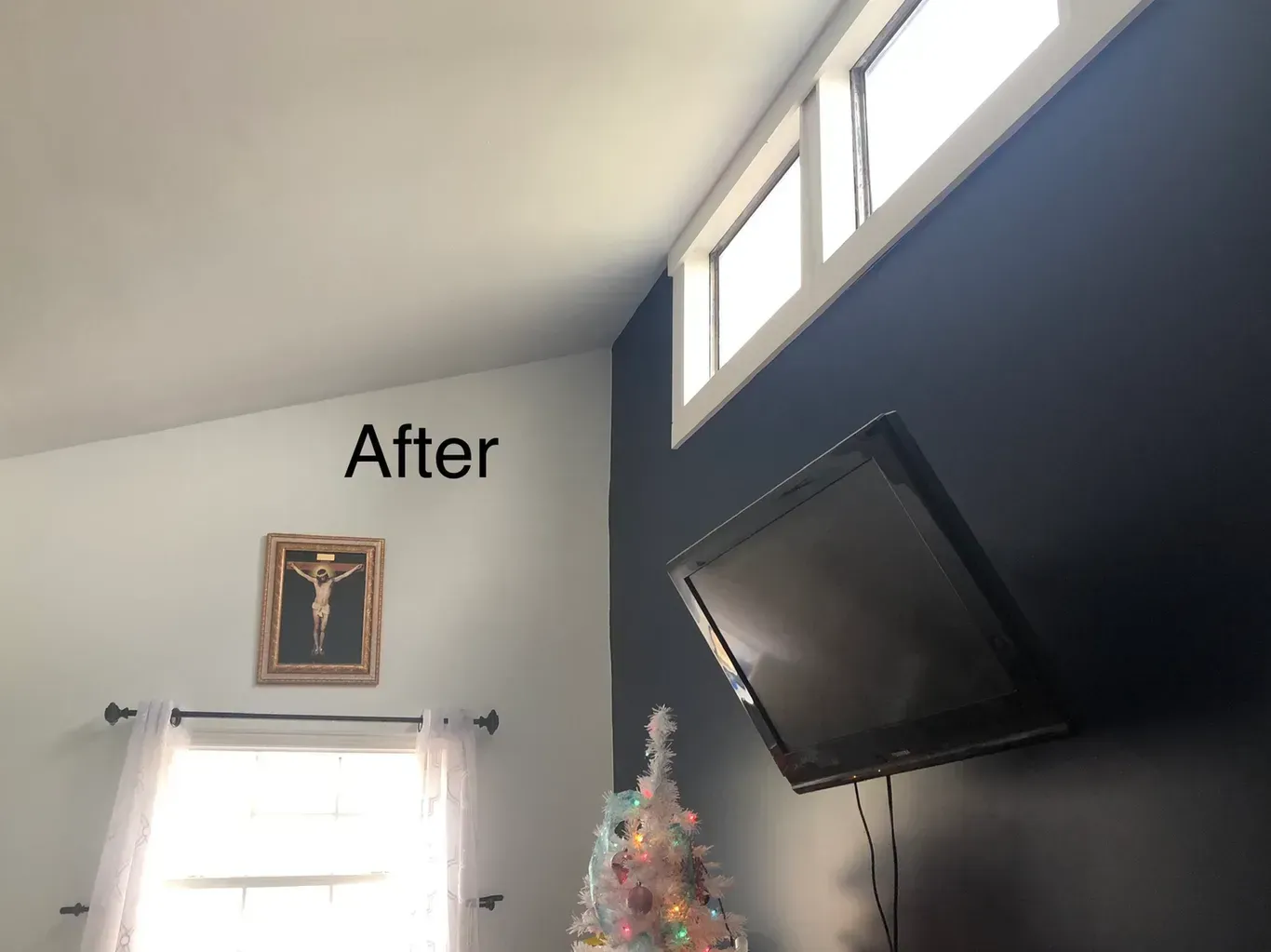 Interior room corner: white ceiling and wall meets a dark blue wall with windows, a TV, and a small Christmas tree.