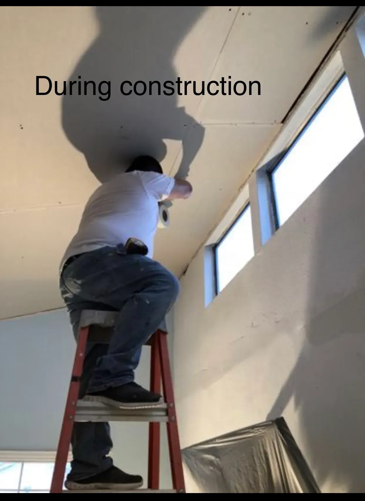Construction worker on a ladder, working on a ceiling near windows. During construction.