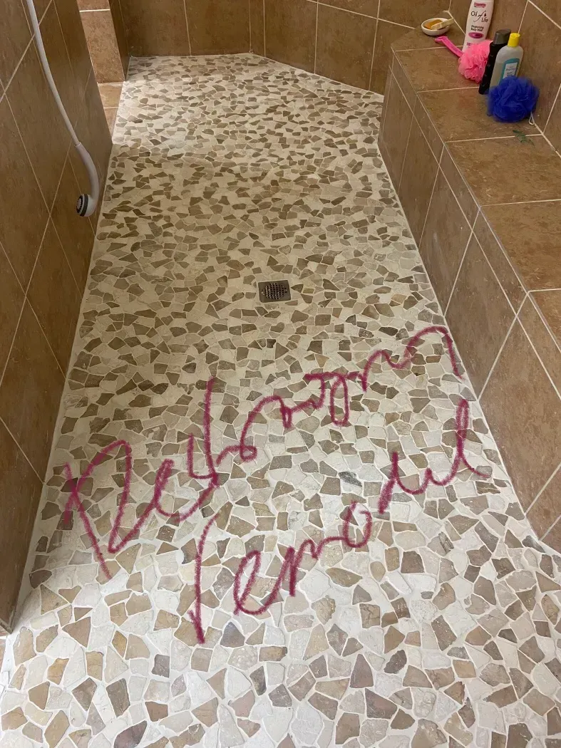 Shower floor with pink graffiti that reads 