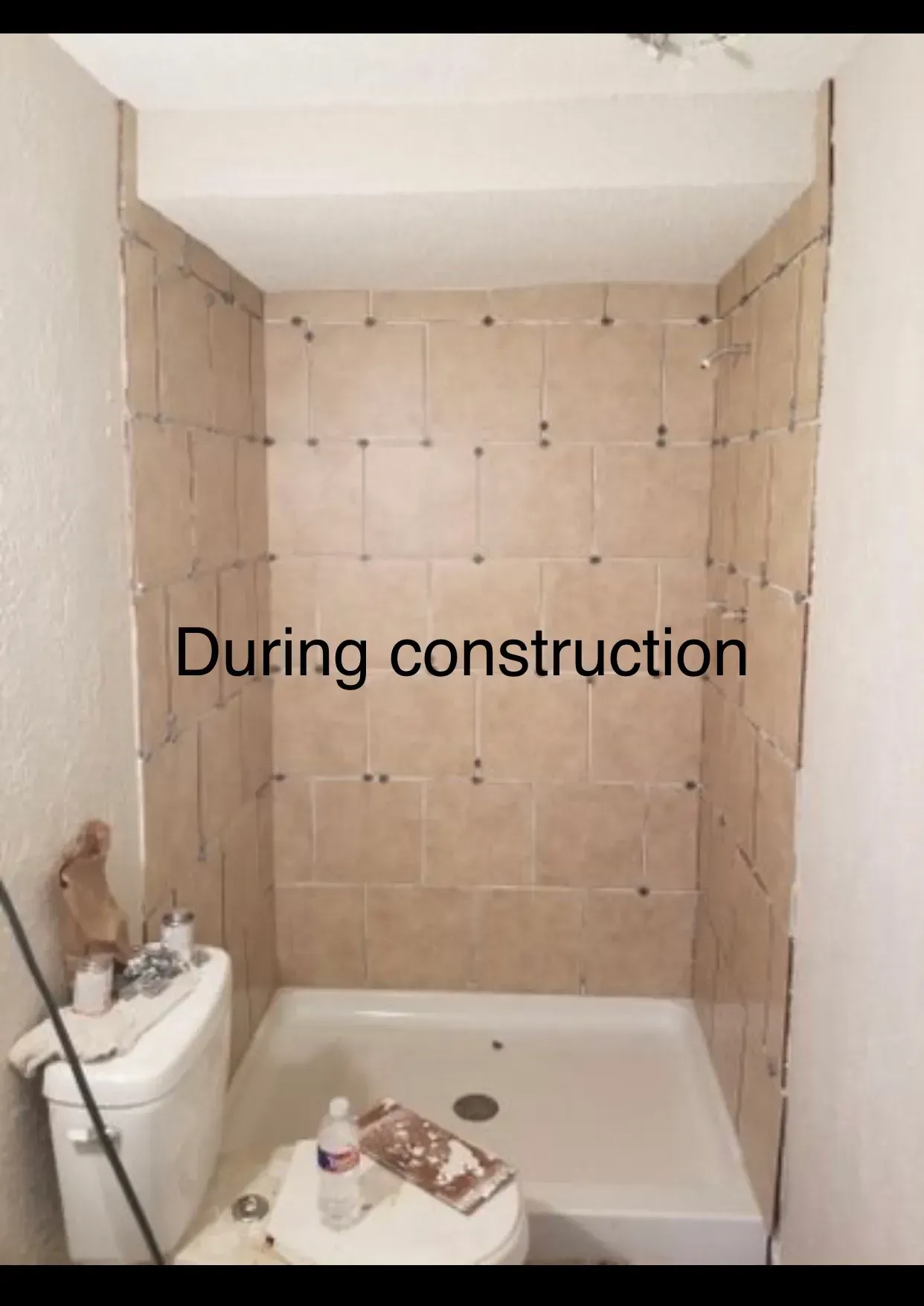 Bathroom under construction: beige tiled shower walls with spacers; white toilet and shower base.