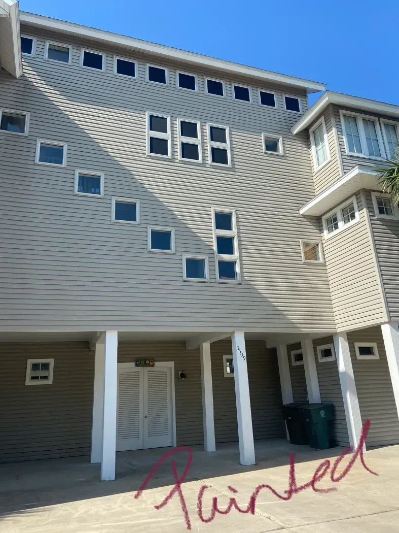 Beige multi-story building with many square windows, supported by white columns, against a blue sky.