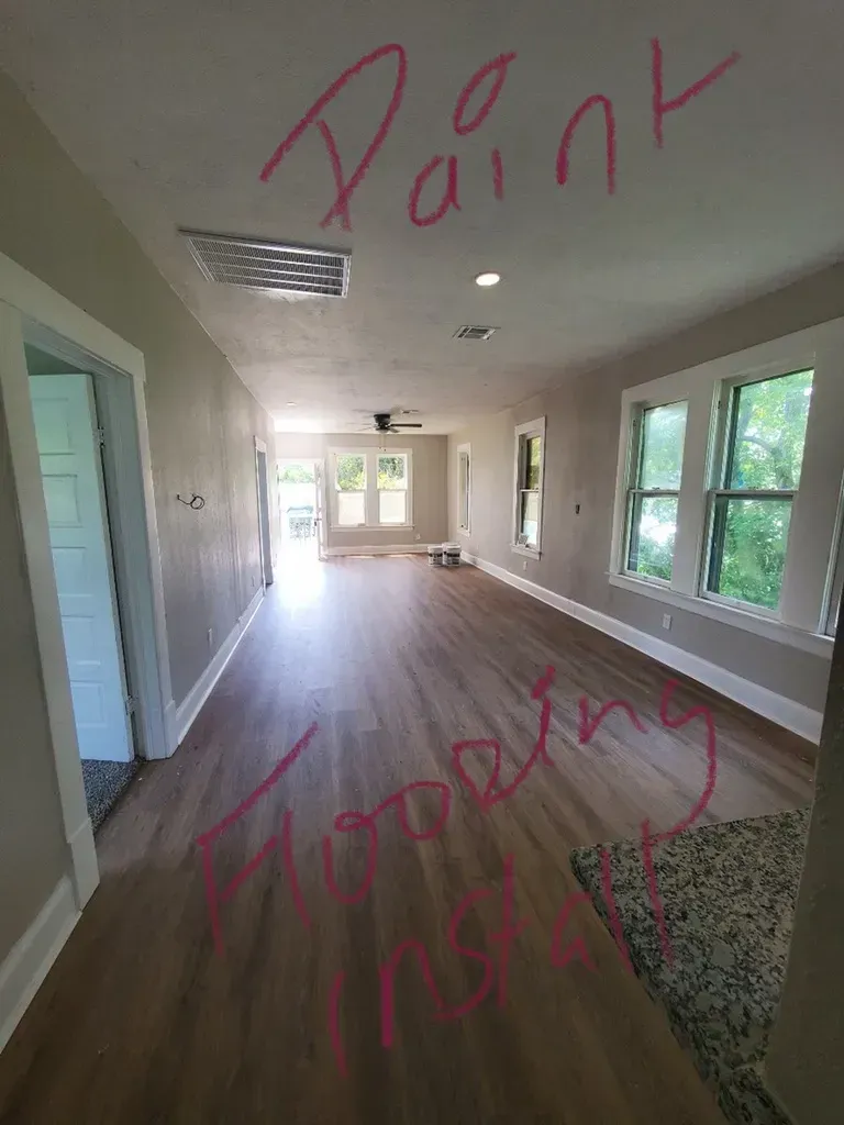 Long, empty living room with hardwood floors, windows, and text 