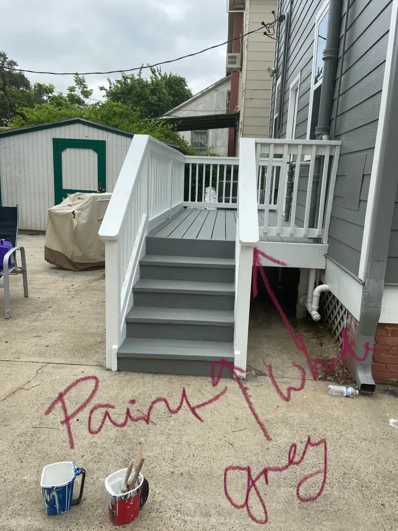 Grey painted deck and steps next to a gray house. White railing. Paint buckets are in the foreground.