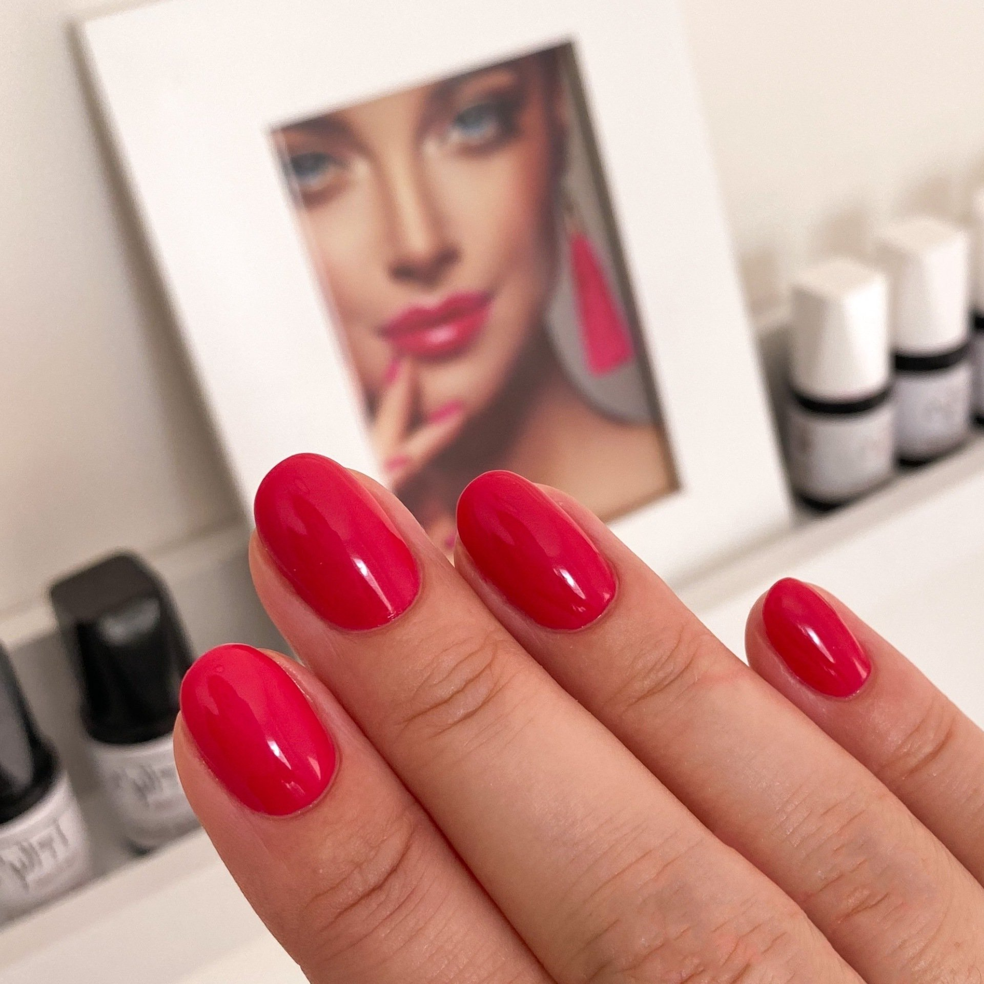 Een vrouwenhand met rode nagels en een foto van een vrouw op de achtergrond