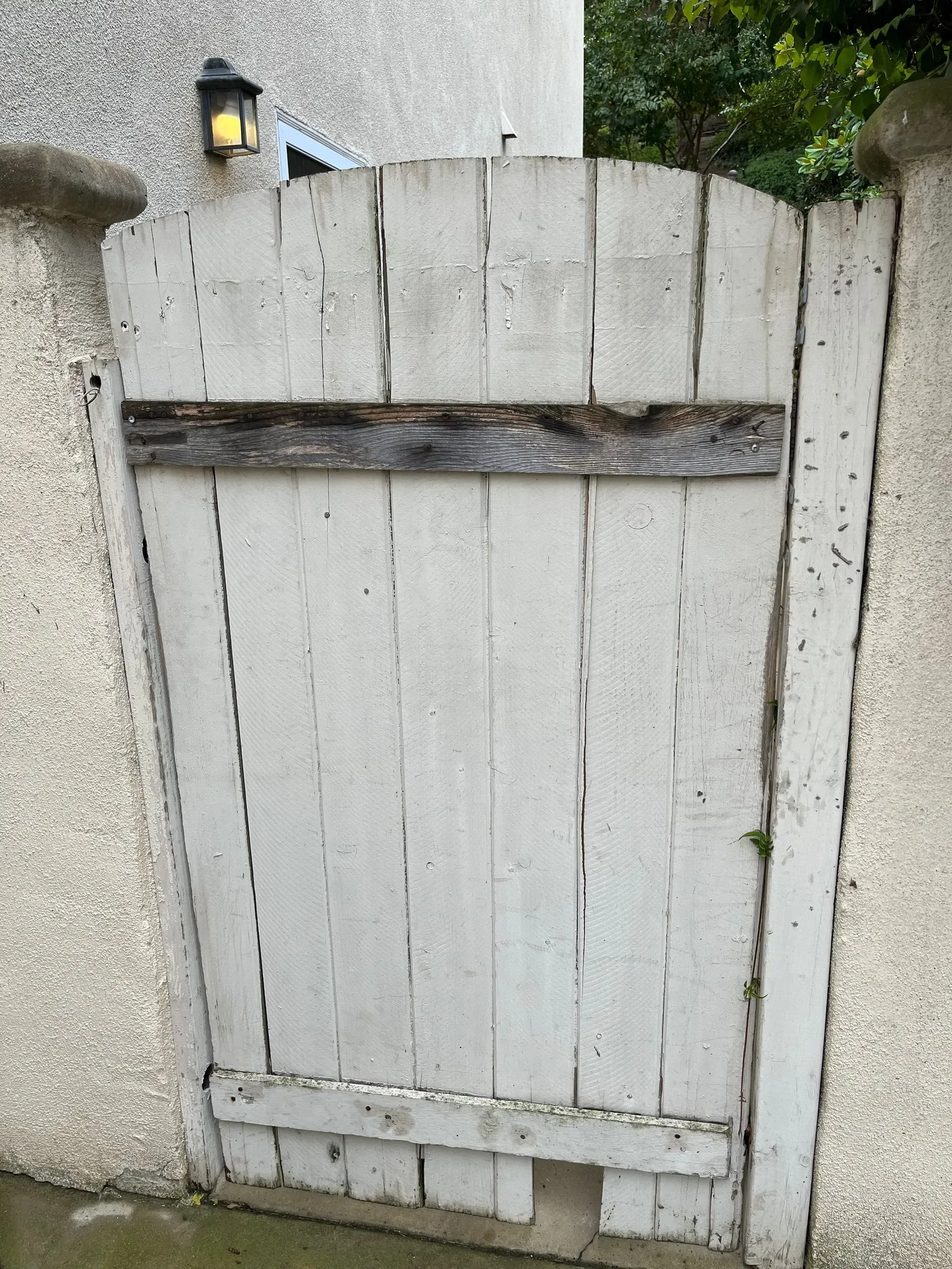 White, weathered wooden gate set between stucco walls, with a dark horizontal board.