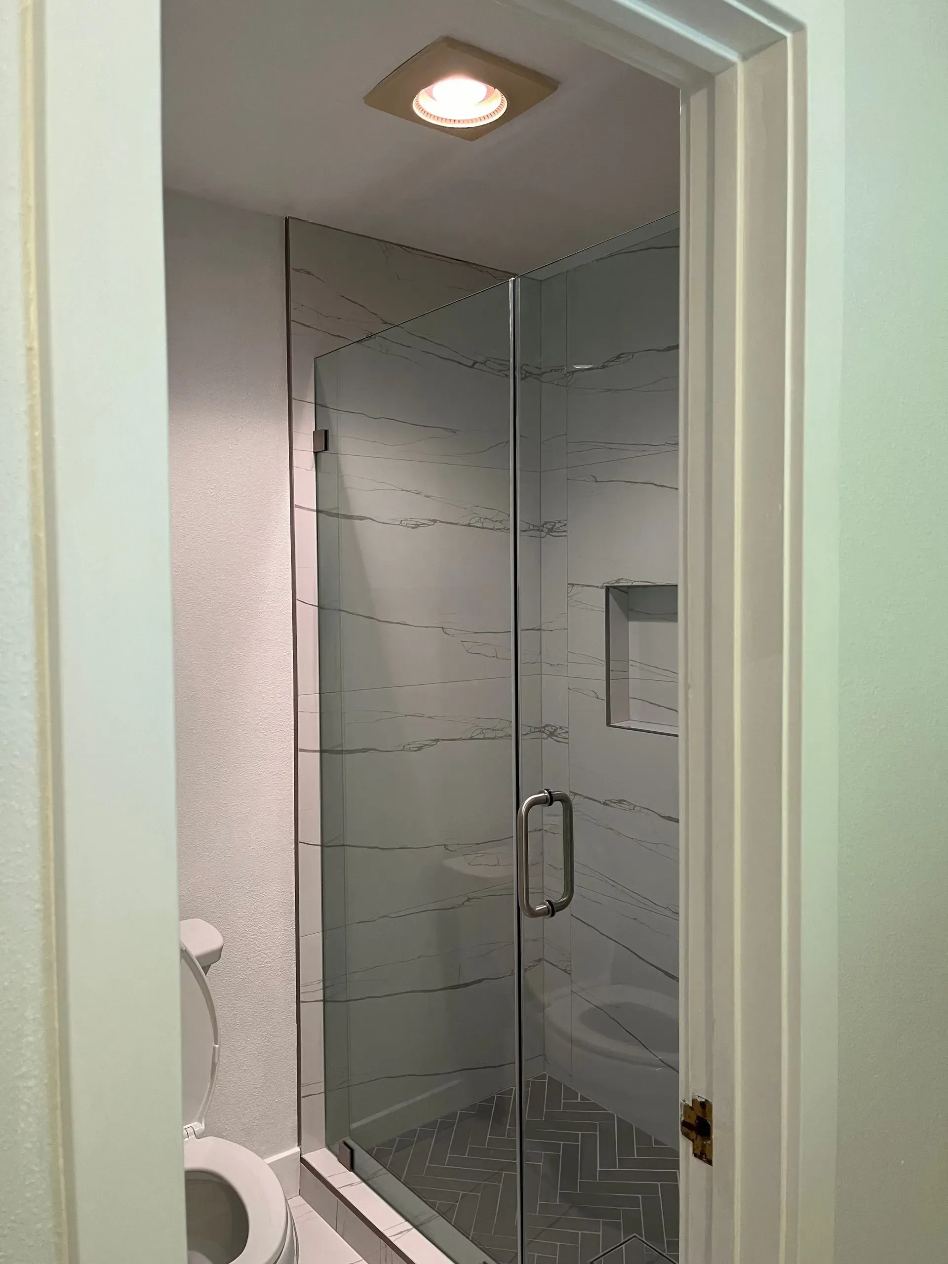 Bathroom with shower enclosure, toilet, and overhead light. White and gray tones dominate the scene.