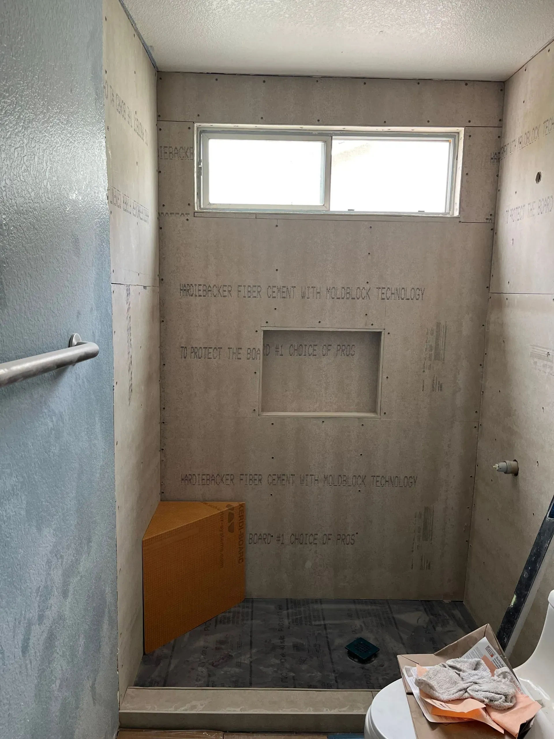A shower under construction with cement walls, a small window, a niche, and a corner seat.