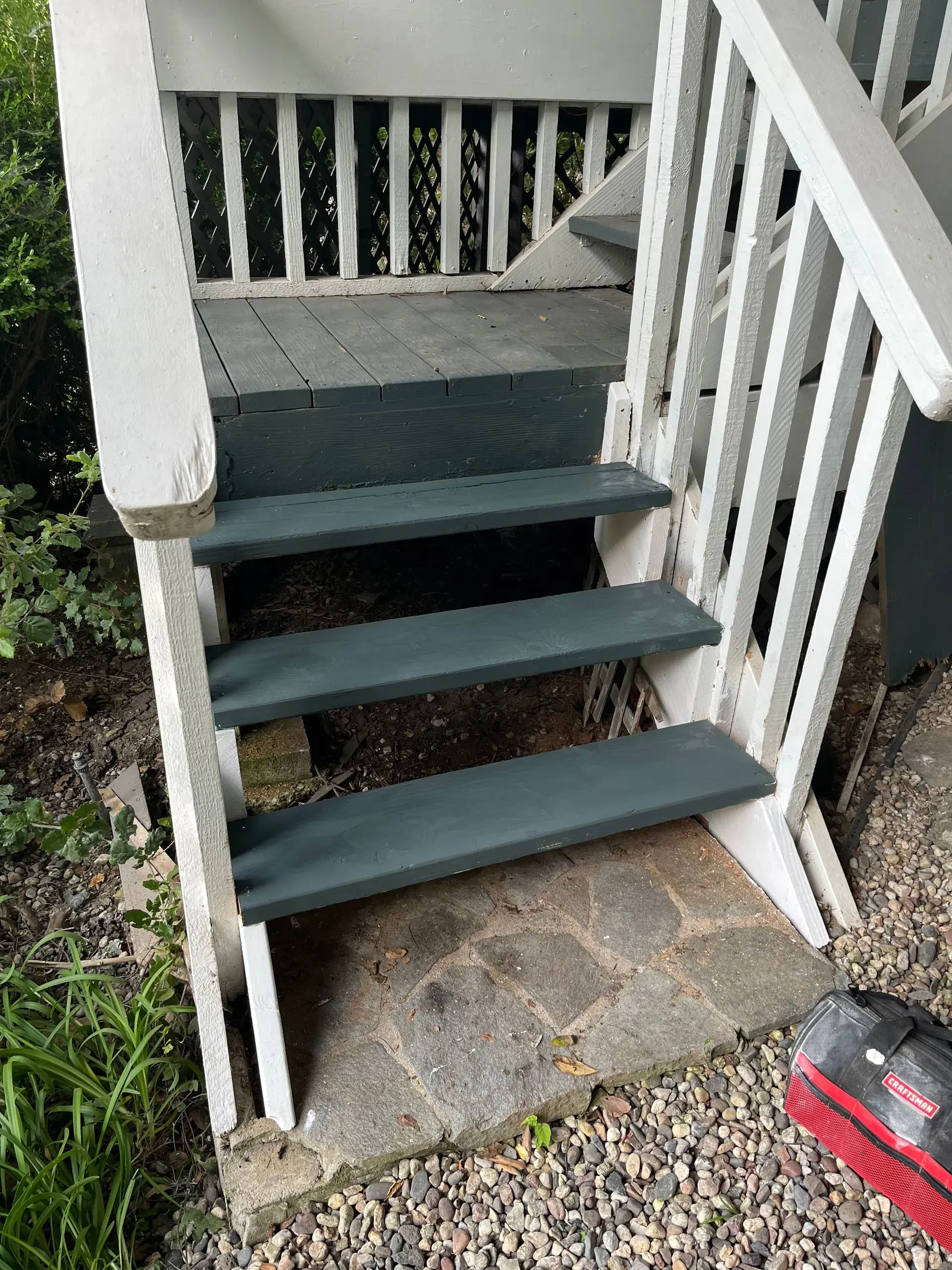 Wooden steps painted green and white, leading up to a porch. Ground is stone and gravel.