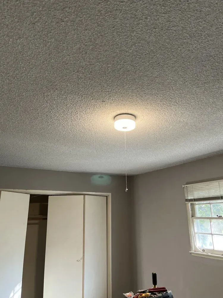 Bedroom interior: white closet doors, gray walls, ceiling light, textured ceiling, window with blinds.