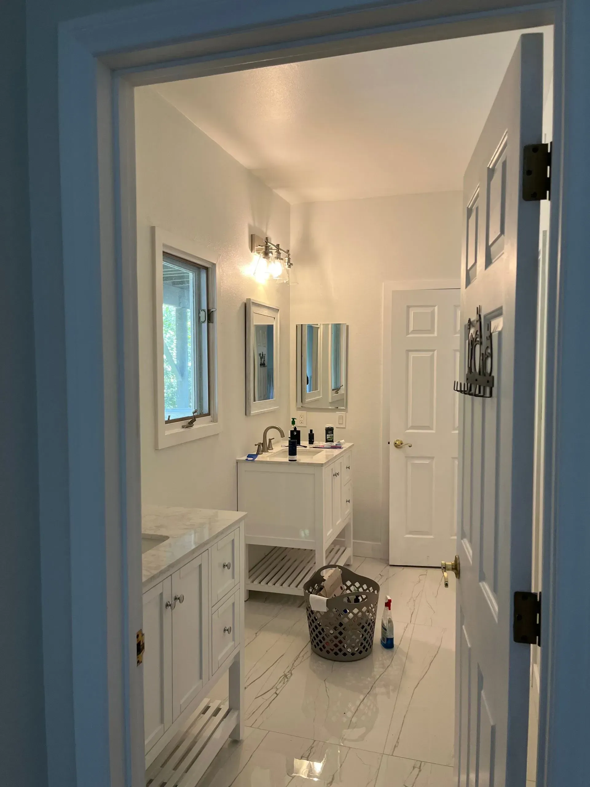 Bathroom interior with white cabinets, marble floors, and a double vanity, viewed through a doorway.
