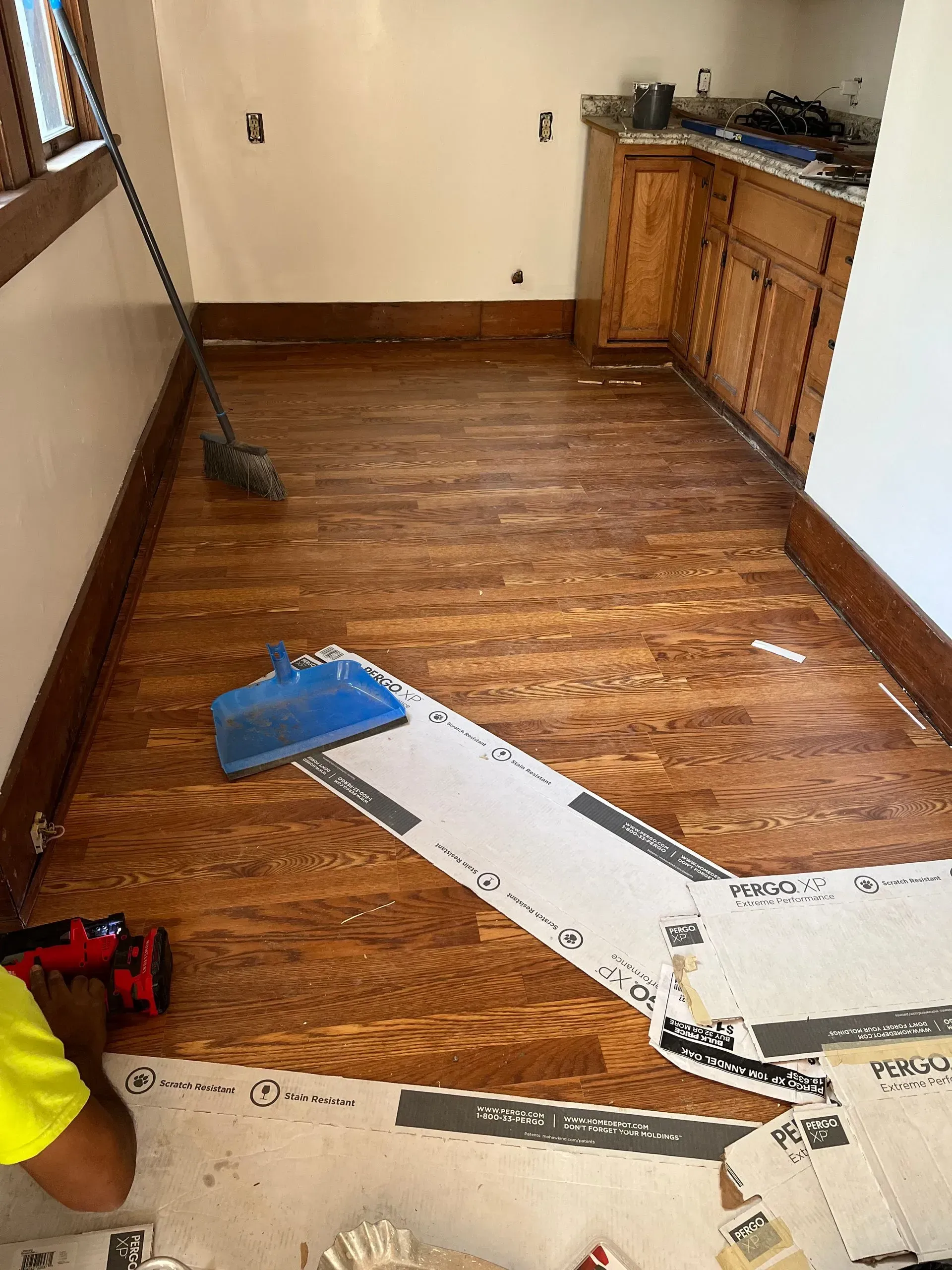 Wood floor being installed in a room with cabinets. A person is working, using protective coverings.