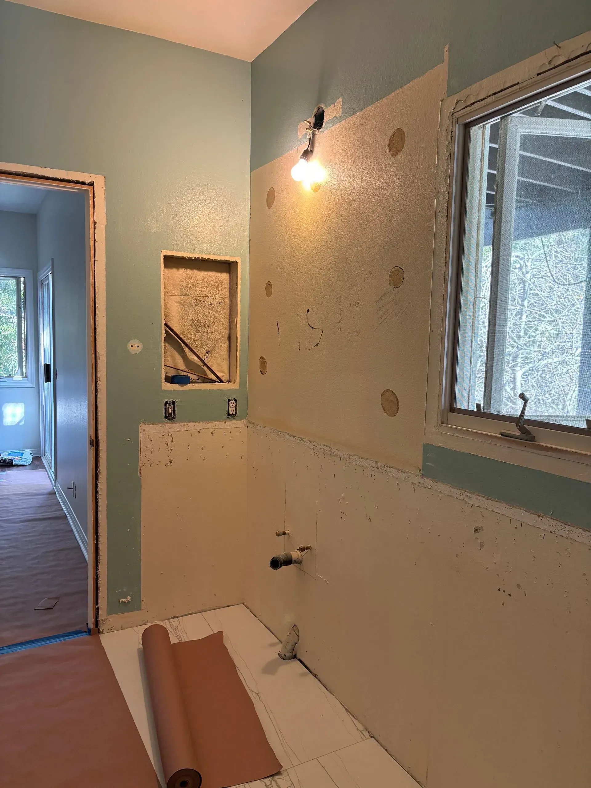 Bathroom renovation in progress with exposed drywall and plumbing. Blue and off-white walls, roll of paper on floor.
