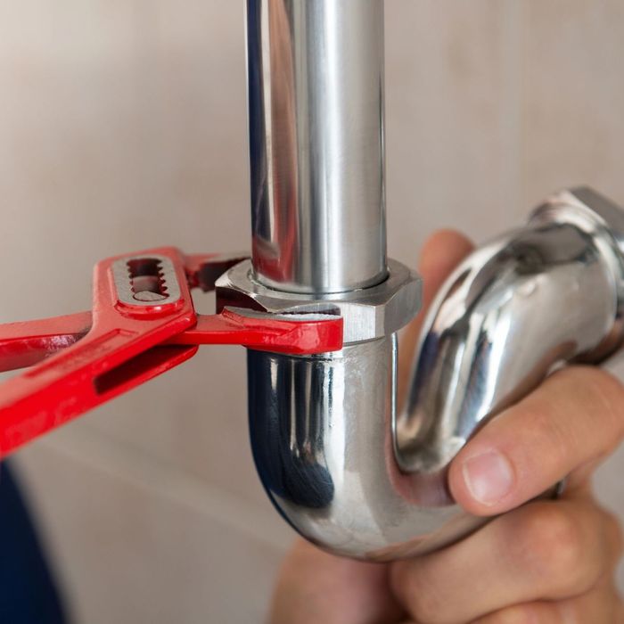 A person is fixing a pipe with a wrench.