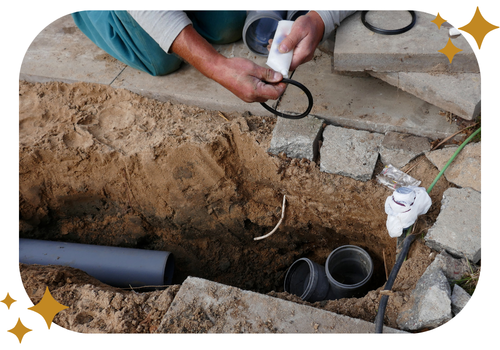 A man is working on a pipe in the dirt.