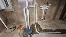 A basement with a sump pump and pipes in it.